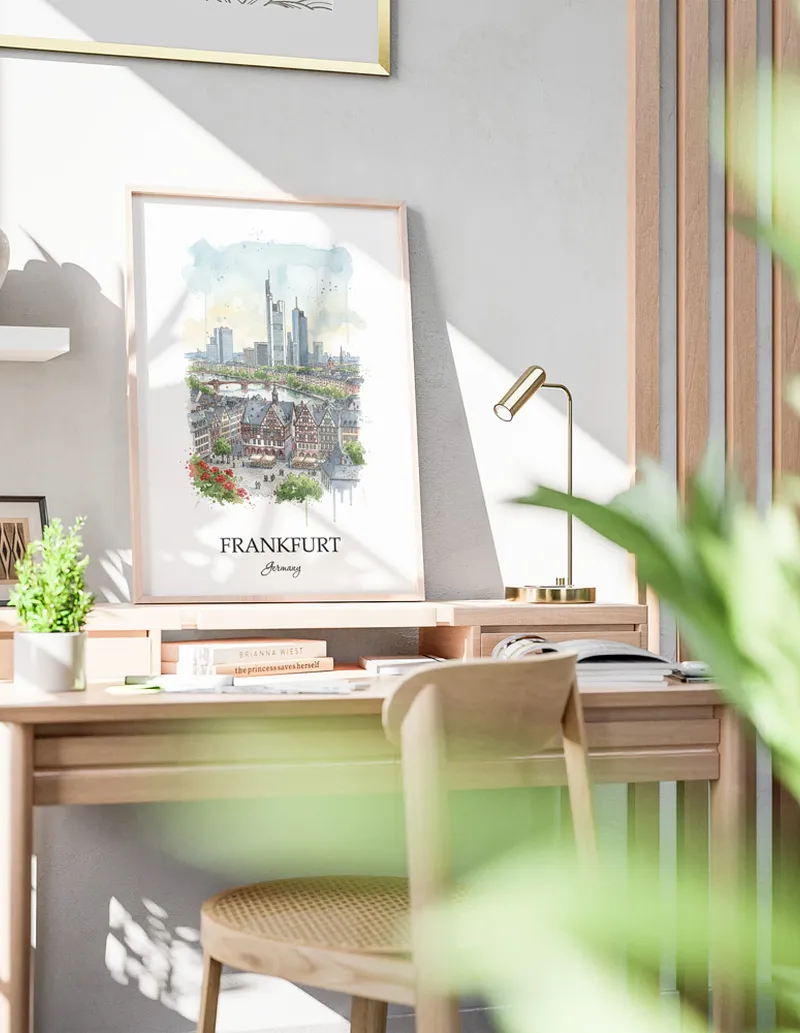 Cozy, well-lit workspace with a minimalist poster of Frankfurt, Germany in a light frame sitting on the desk.