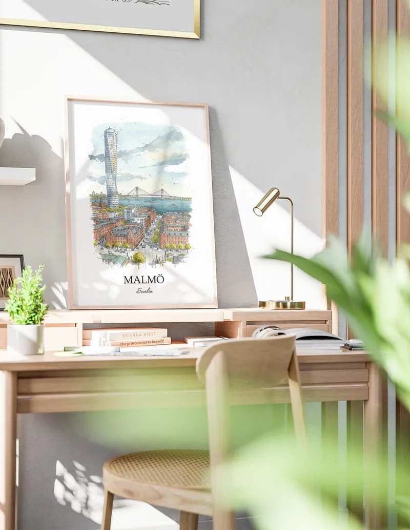 Cozy, well-lit workspace with a minimalist poster of Malmö, Sweden in a light frame sitting on the desk.