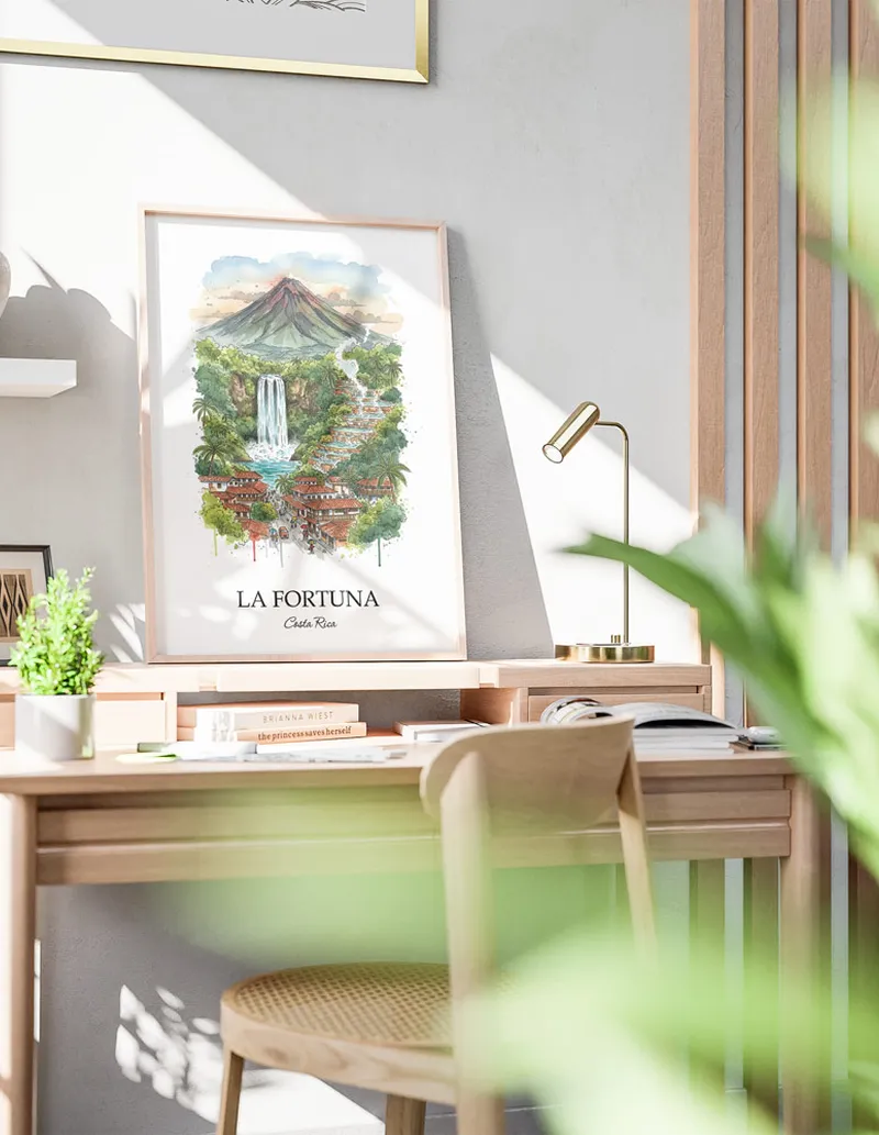 Cozy, well-lit workspace with a minimalist poster of La Fortuna, Costa Rica in a light frame sitting on the desk.