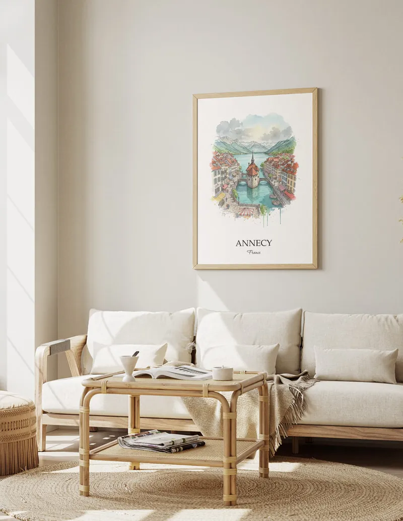 Framed wall art featuring Annecy, France in a light wood frame hanging above a sofa in a modern living room.