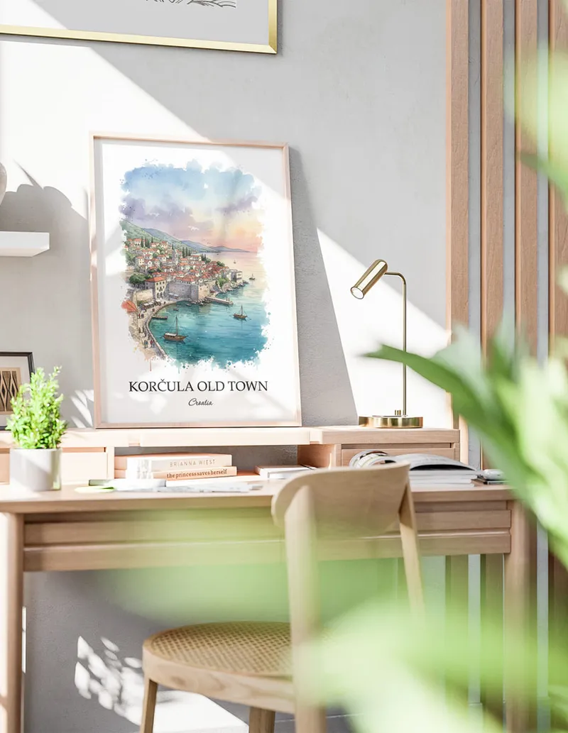 Cozy, well-lit workspace with a minimalist poster of Kor_ula Old Town, Croatia in a light frame sitting on the desk.