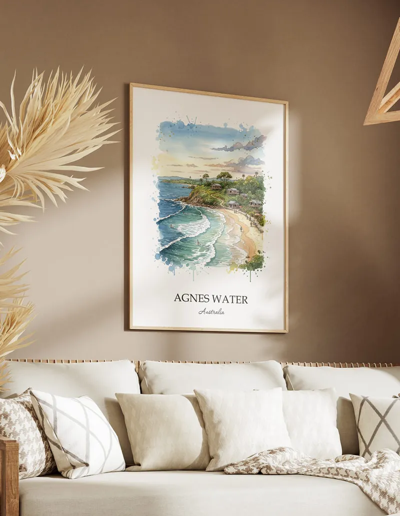 Minimalist poster of Agnes Water in Australia in a light frame standing on the floor in a dark moody interior.