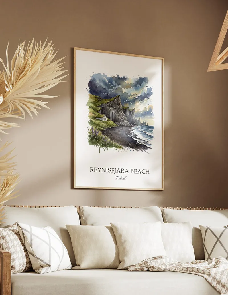 Vintage travel poster of Reynisfjara Beach, Iceland in a light frame displayed above a sofa in a bright boho interior.