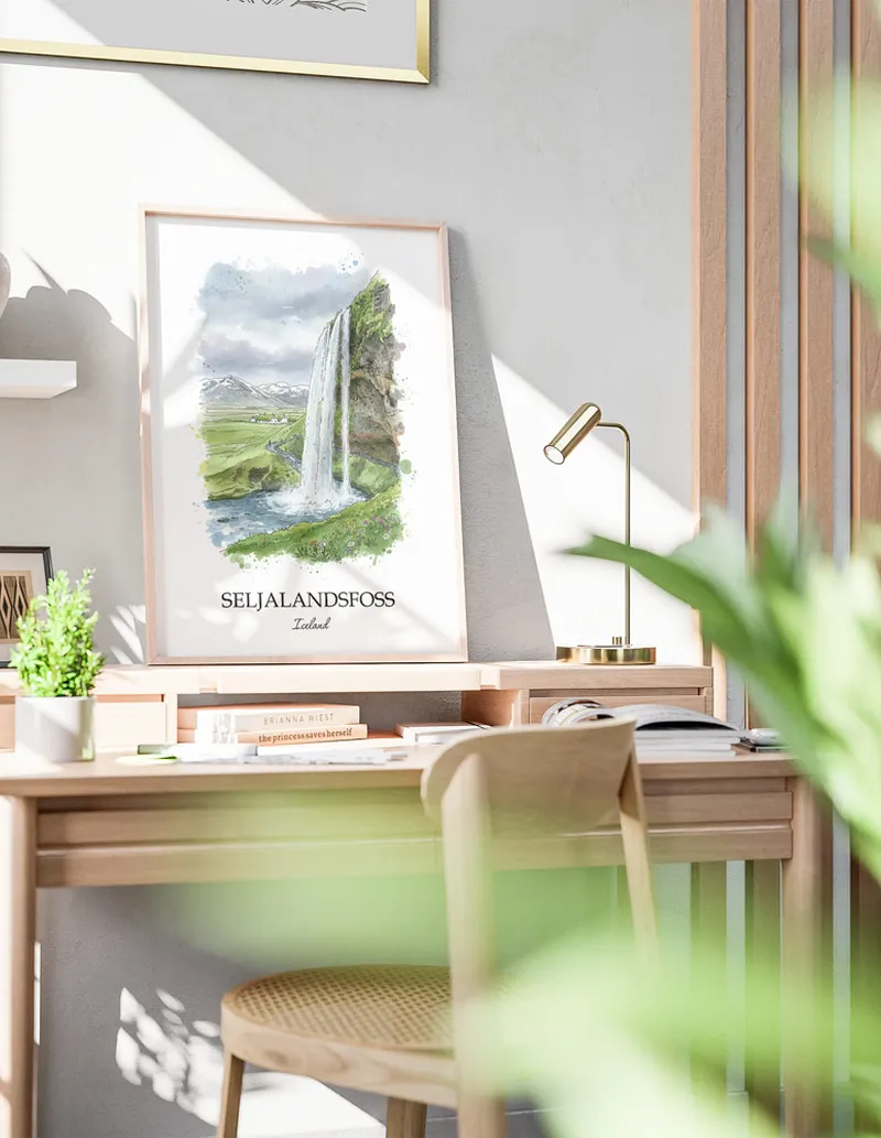 Cozy, well-lit workspace with a minimalist poster of Seljalandsfoss, Iceland in a light frame sitting on the desk.
