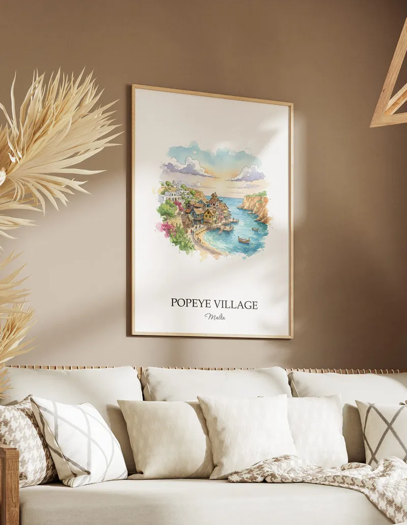 Vintage travel poster of Popeye Village, Malta in a light frame displayed above a sofa in a bright boho interior.