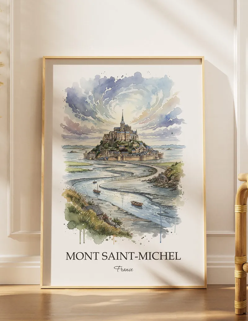 Framed wall art featuring Mont Saint-Michel in France in a light wood frame leaning on the floor.